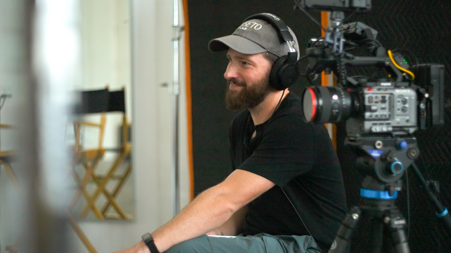 Producer in headphones and a Roseto Films cap beside a cinema camera on set