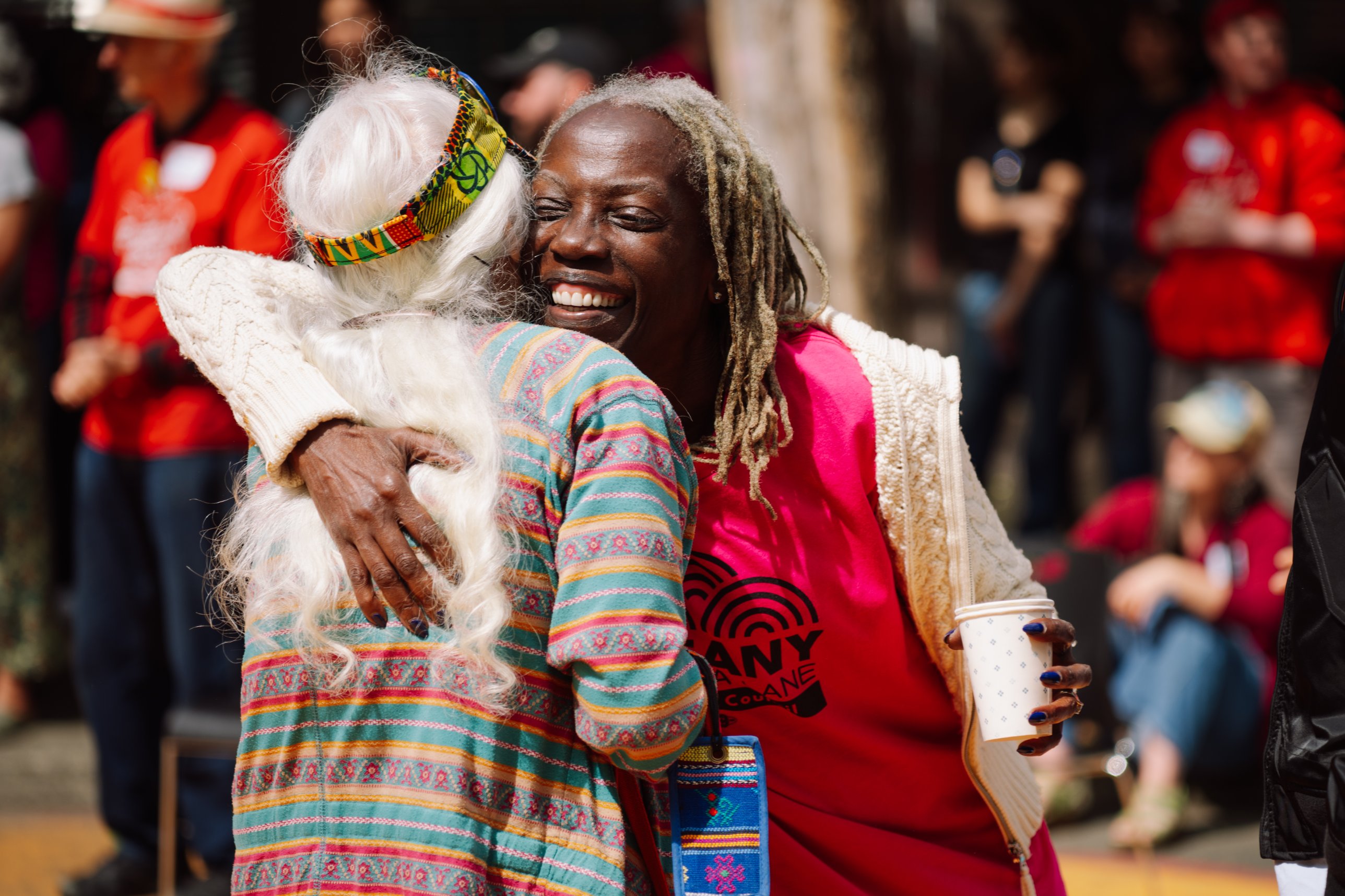 Two community members sharing a joyful hug at an outdoor gathering